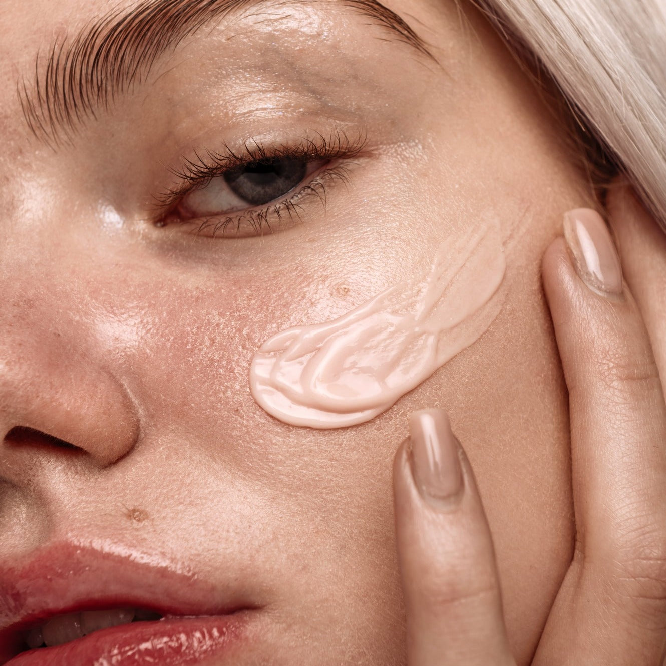 Close up of young Caucasian model with pinkish cream spread on her cheek.