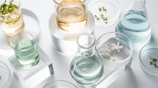 Glass beakers and petri dishes filled with colorful liquids and botanical elements, representing natural skincare ingredients.