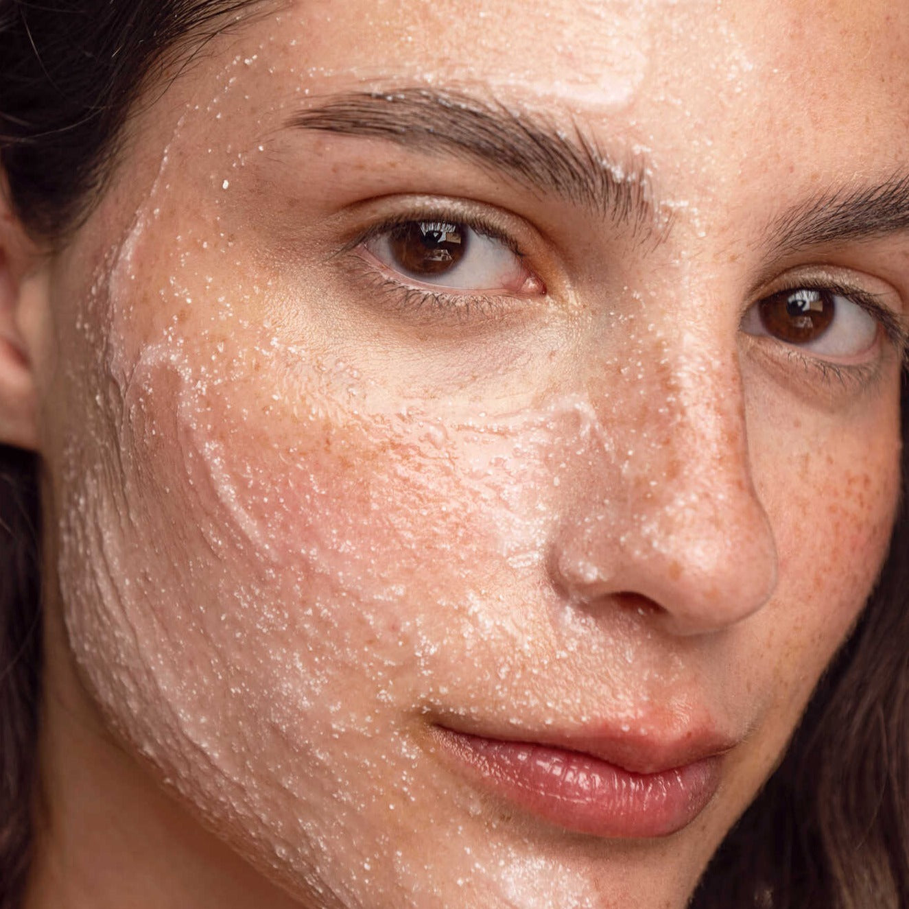 Young Caucasian woman looking at the camera with her face covered with the exfoliating mask.