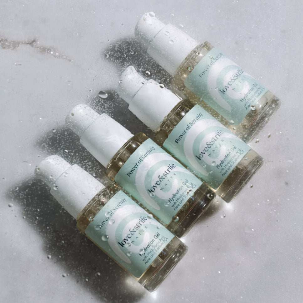 Four bottles of love&strife's Hydration Gel on a wet marble surface, highlighting their moisturizing skincare benefits.