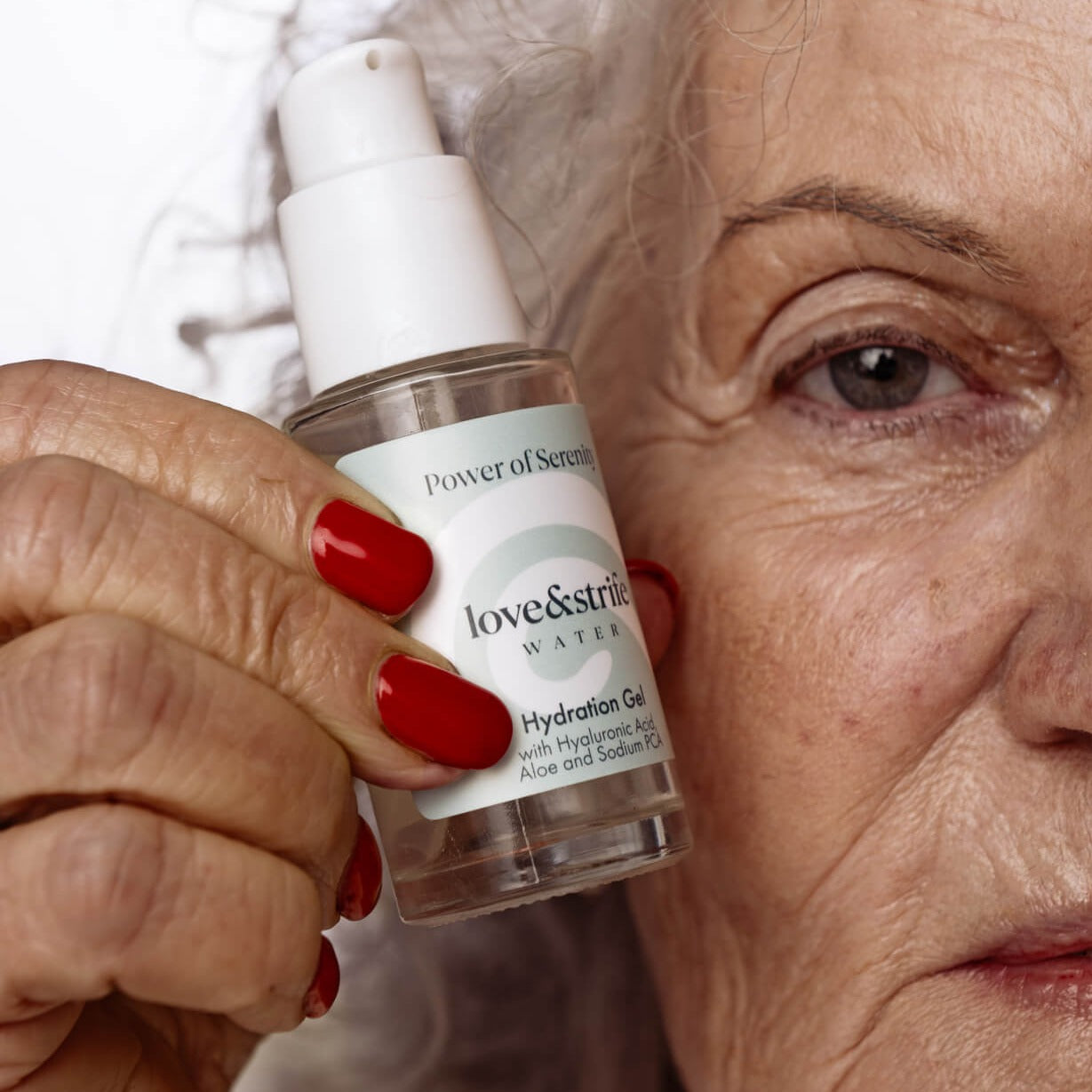 Close-up of senior woman with red nails holding love&strife's Hydration Gel bottle near her face