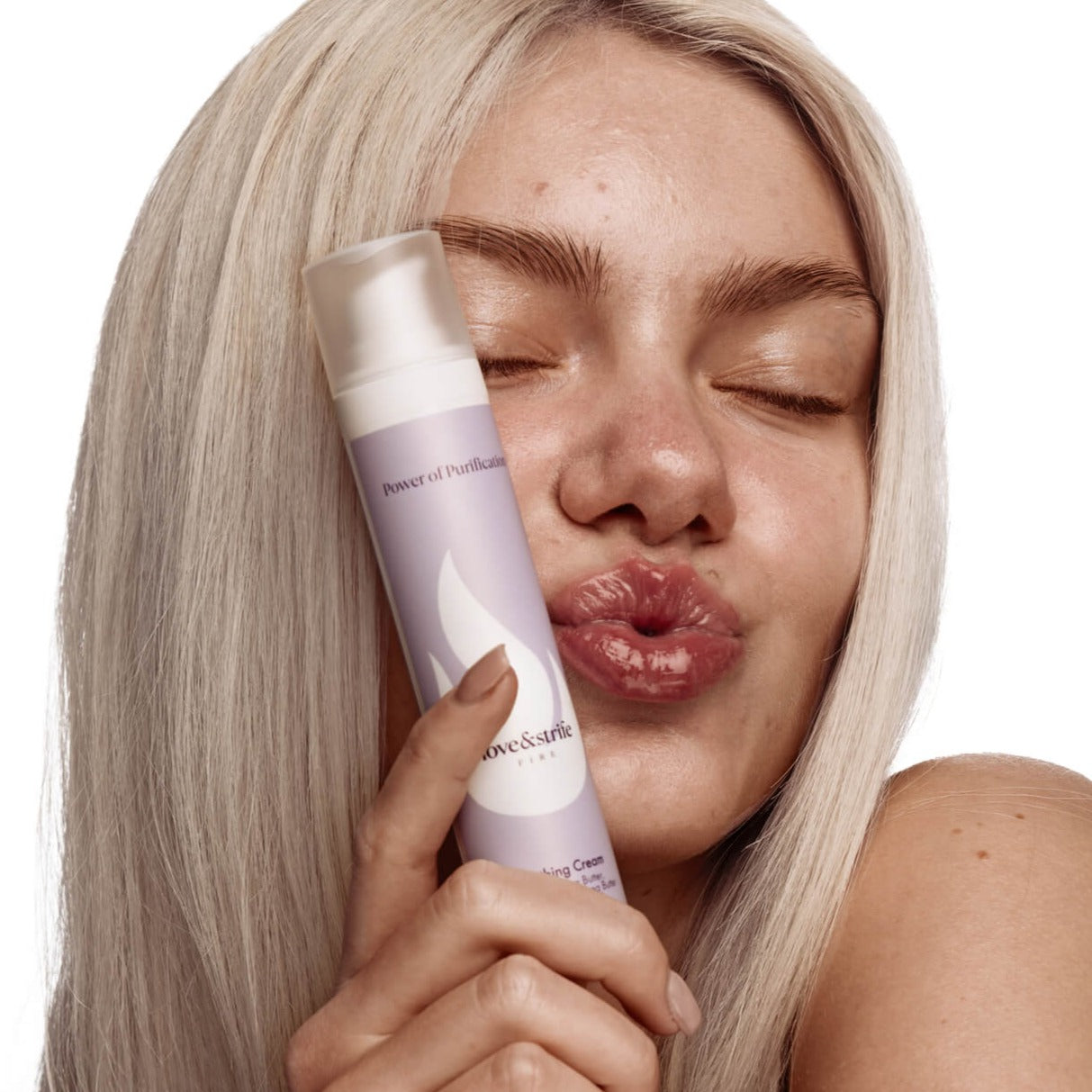 Young Caucasian woman holding the Soothing Cream by love&strife close to her face with her eyes closed and her lips forming a kiss.