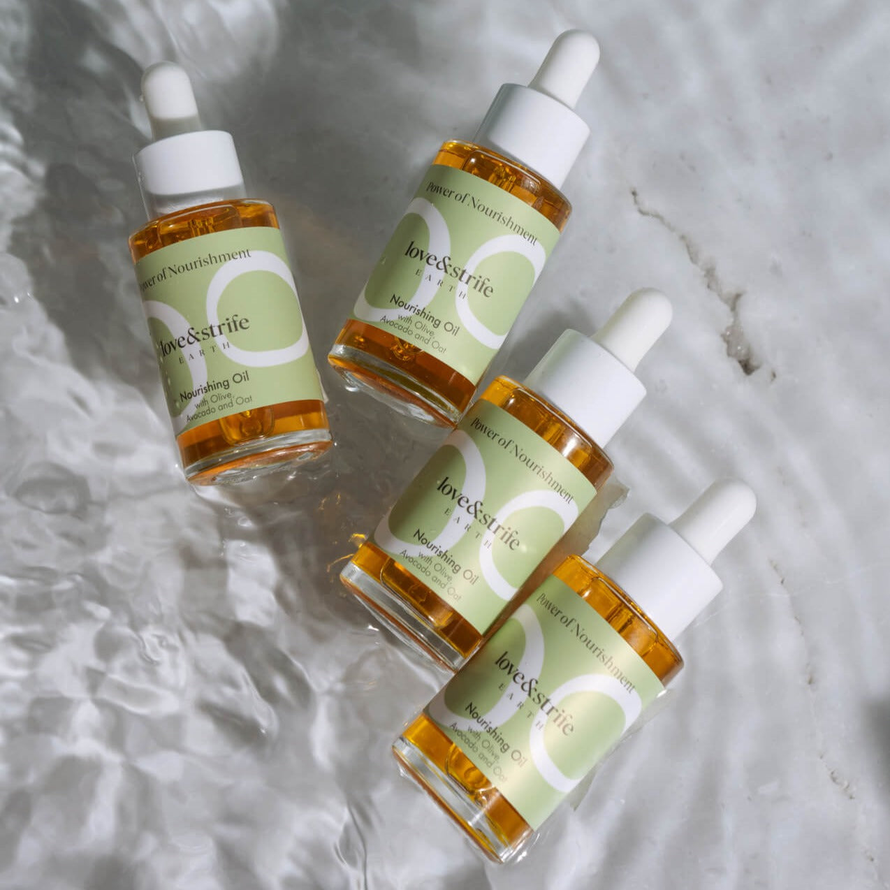 Four bottles of love&strife's Nourishing Oil on a wet marble surface, perfect for moisturizing and rejuvenating skincare routines.