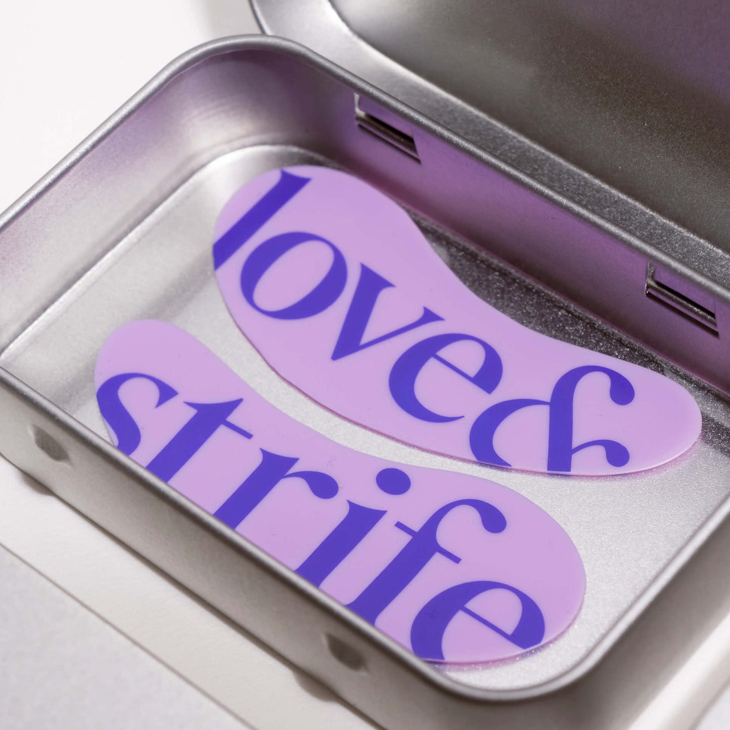 Reusable silicone eye patches displayed inside an open metal case featuring the love&strife logo.